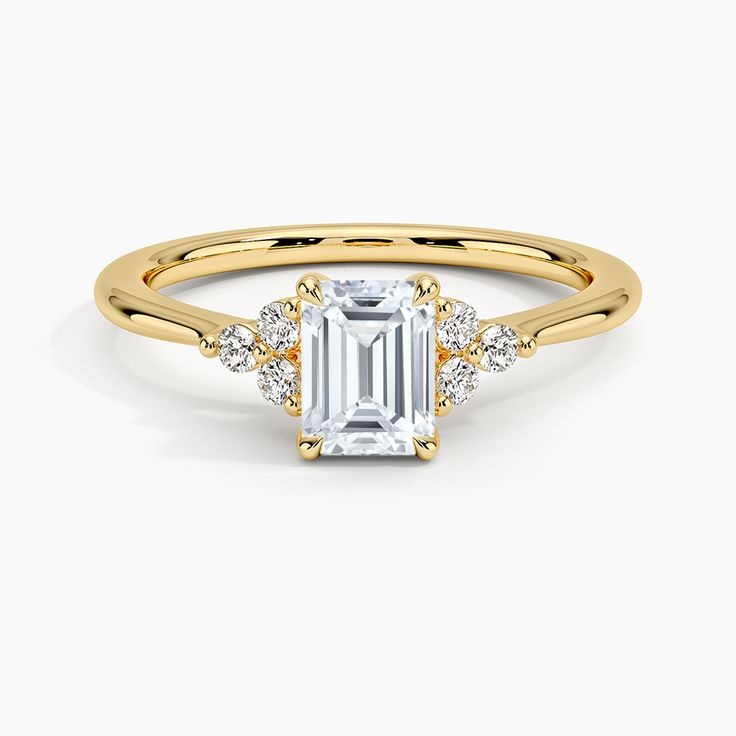 Emerald Cut Melody Diamond Engagement Ring - 18K Yellow Gold. This chic ring features a dazzling cluster of three diamonds framing each side of the center gem. The gently tapering band and open gallery creates a light and lustrous look (1/10 total carat weight). 14k Gold Cluster Diamond Ring With Prong Setting, Fine Jewelry Promise Ring With Emerald Cut Cluster, Dazzling Moissanite Cluster Ring With Emerald Cut, Yellow Gold Diamond Ring With Brilliant Cut Cluster, Cluster Yellow Gold Diamond Ring With Prong Setting, Yellow Gold Cluster Diamond Ring With Prong Setting, 14k Gold Cluster Diamond Promise Ring, Dazzling Emerald Cut Moissanite Cluster Ring, Elegant Yellow Gold Cluster Diamond Ring