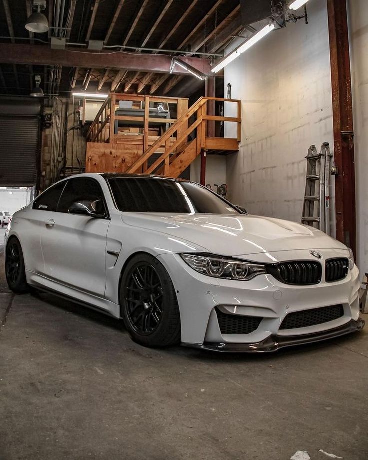 a white car parked in a garage next to a stair case and some stairs on the wall