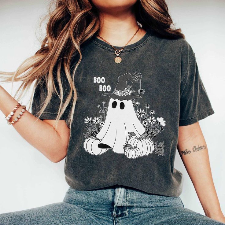 Trendy women's t-shirt with a super cute and creative "BOO BOO" Halloween design. This t-shirt is made from soft and breathable cotton, ensuring absolute comfort while wearing. The standout print features a small ghost wearing a witch hat, surrounded by flowers and two pumpkins, creating a youthful and unique look. * Made with medium fabric (5.3 oz/yd² (180 g/m consisting of 100% cotton for year-round comfort that is sustainable and highly durable. * The classic fit of this shirt ensures a comfy, relaxed wear while the crew neckline adds that neat, timeless look that can blend into any occasion, casual or semi-formal. If you would like to choose a different color for the shirt, please don't hesitate to message the shop. We will assist you if we have that color available. This product is ma Halloween Novelty Cotton T-shirt, Spooky T-shirt With Funny Print In Relaxed Fit, Trendy Halloween Graphic T-shirt, Trendy Halloween Crew Neck T-shirt, Casual Halloween T-shirt With Letter Print, Trendy Halloween Short Sleeve T-shirt, Spooky Relaxed Fit T-shirt With Funny Print, Casual Halloween Letter Print T-shirt, Funny Cotton Halloween T-shirt