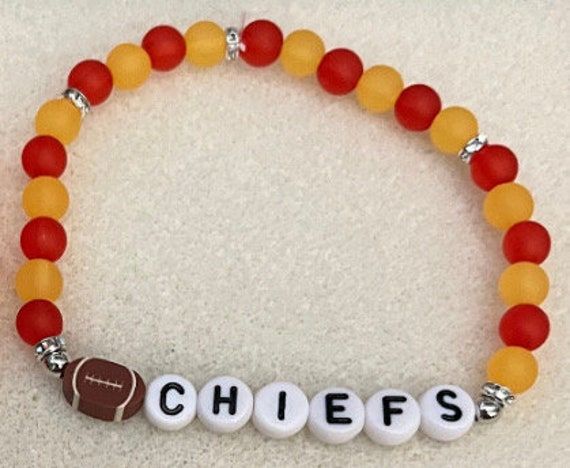 Support the Chiefs year-round with this cute, lightweight bracelet! Made with round beads, silver rhinestone spacers and a football charm.   For sizing help:  6 inches is considered a child or an adult X-small wrist. 6.5 inches is considered an adult small wrist. 6.75 inches is considered an adult medium wrist. 7 inches is considered an adult large wrist. 7.25 inches is considered an adult X-large wrist. Personalized Orange Round Bead Jewelry, Personalized Red Name Bracelet With Round Beads, Red Beaded Name Bracelet With Round Beads, Red Beaded Name Bracelet, Adjustable Red Name Bracelet With Round Beads, Red Beaded Charm Bracelet For Friendship, Red Letter Beads Jewelry, Red Jewelry With Round Letter Beads, Red Bracelets With Letter Beads