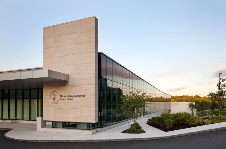 the building has many windows and plants on it's front side, along with an empty parking lot