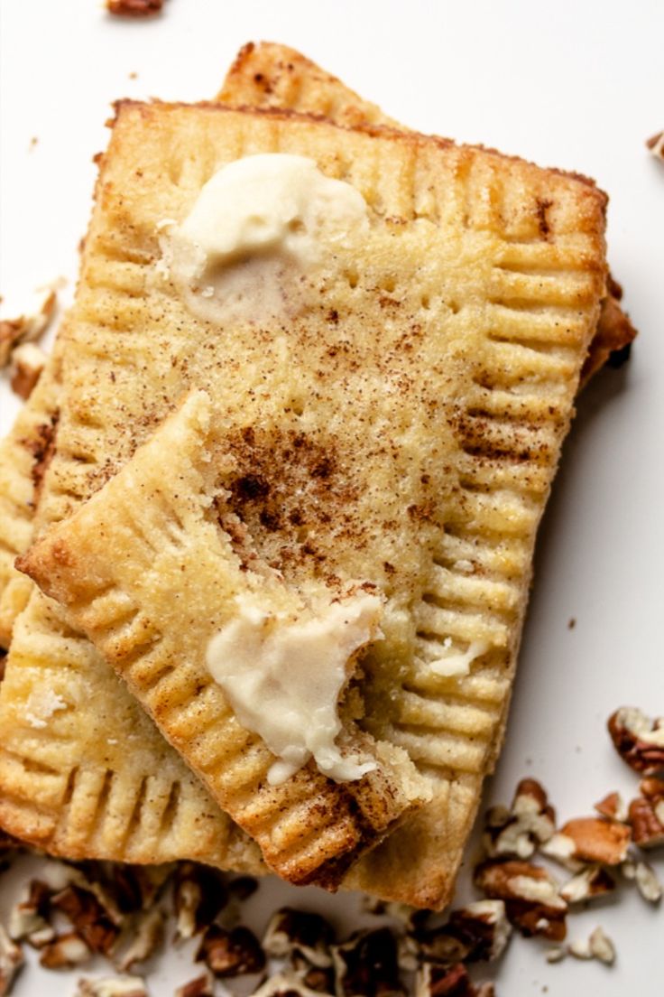 two pieces of pie with cream on top and chopped nuts around it, sitting on a white surface