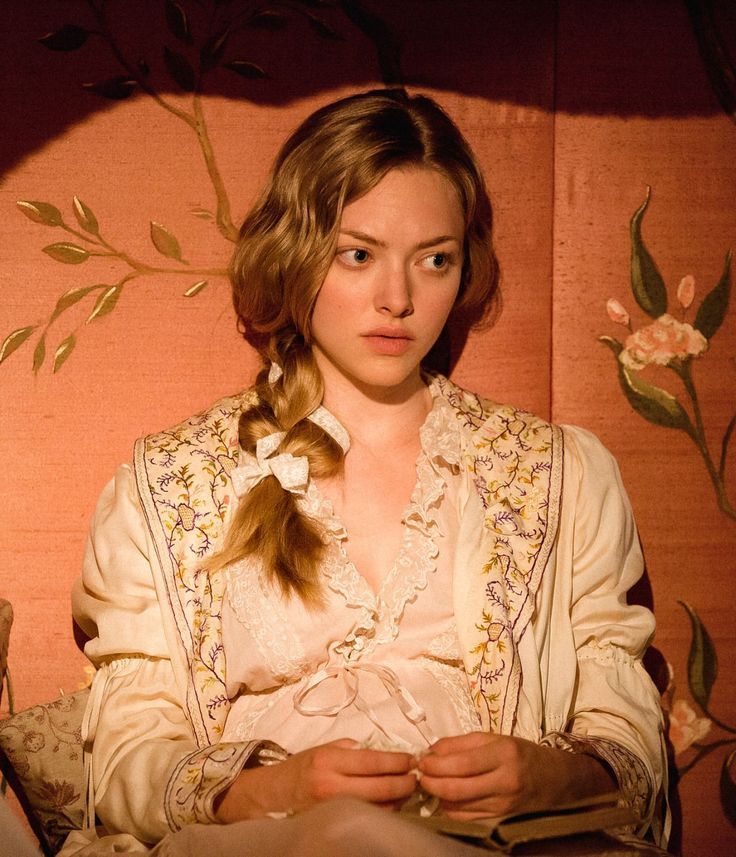 a woman sitting in front of a wall with flowers on it and her hands folded