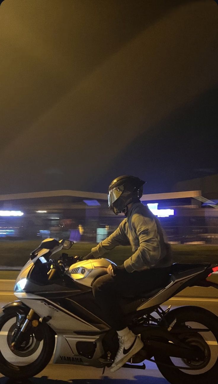 a man riding on the back of a motorcycle down a street at night with traffic lights in the background