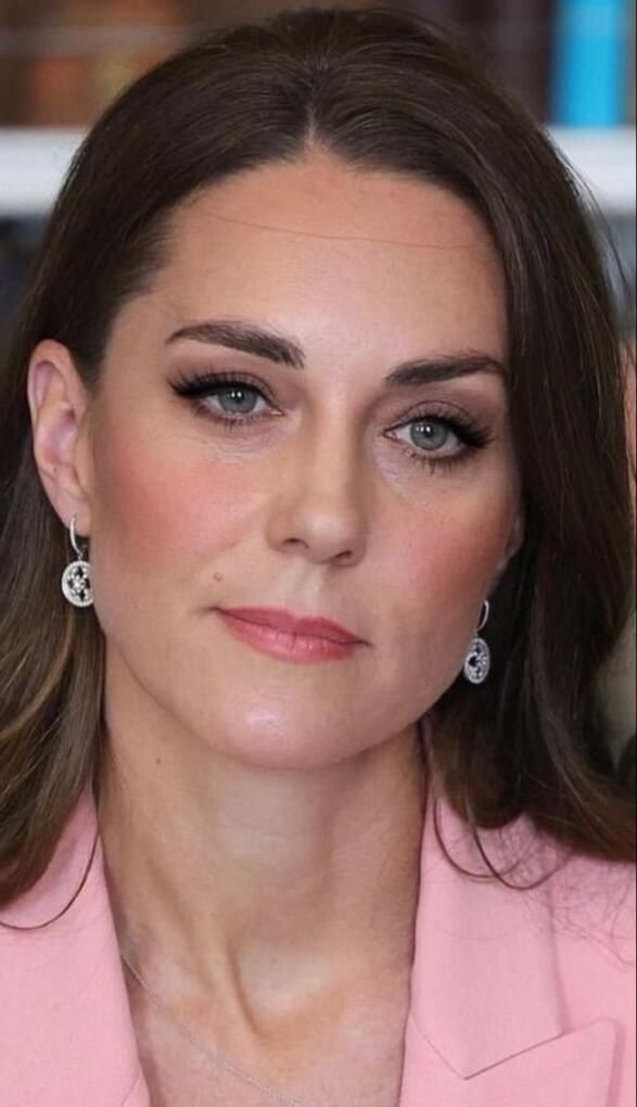 a woman in a pink suit and earrings looking at the camera