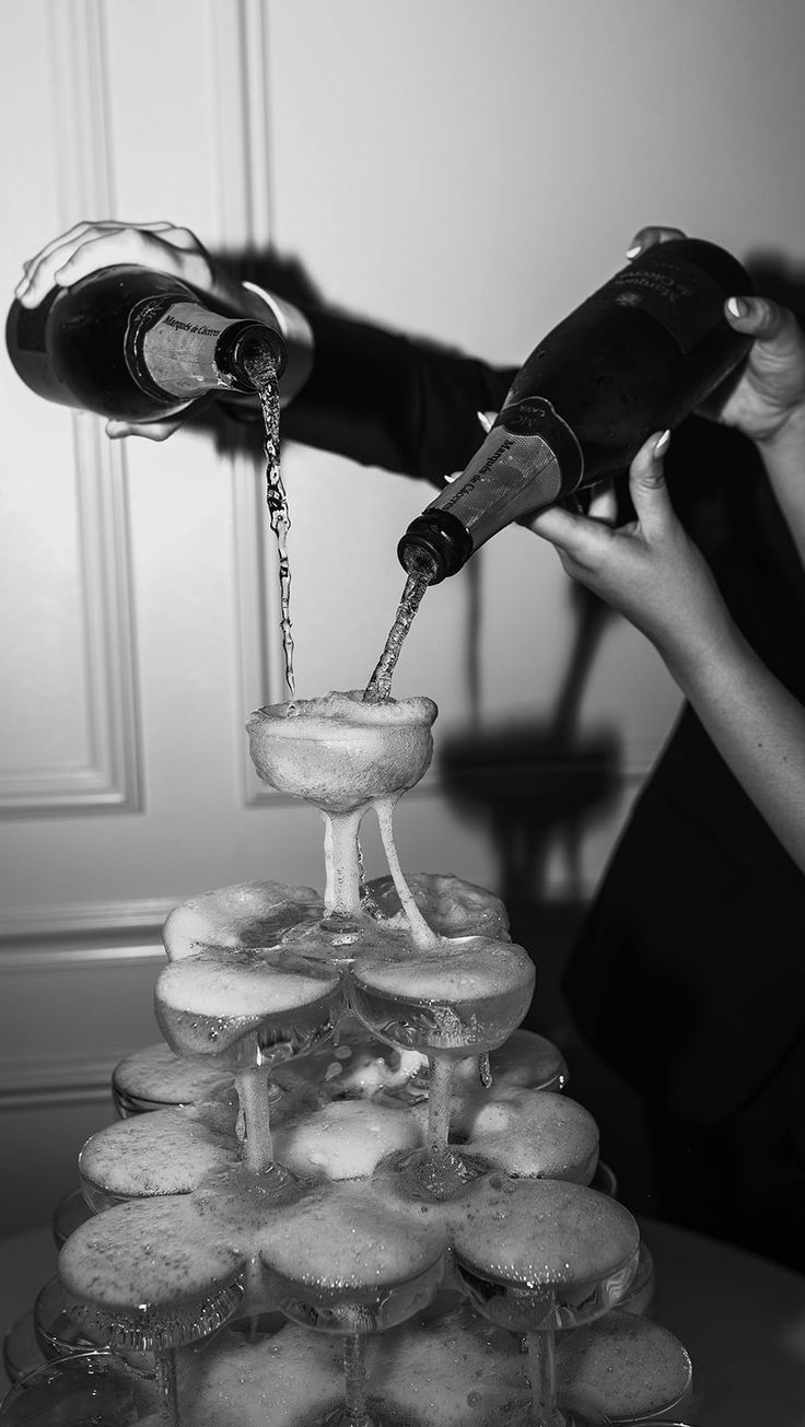 a woman pours champagne on top of a tower of doughnuts in black and white