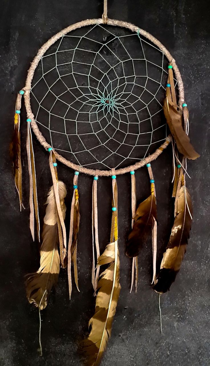 a dream catcher with feathers hanging from it's side on a black wall background