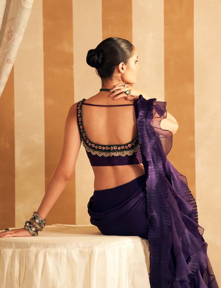 Enchant in the purple net embroidered sleeveless blouse paired with a chiffon organza double draped ruffle sari. The sleeveless blouse features intricate net embroidery in a regal purple hue, exuding sophistication. The sari, crafted from chiffon and organza, boasts a unique double draped ruffle design that flows gracefully, adding a touch of modern elegance. This ensemble beautifully blends classic charm with contemporary flair, perfect for any elegant occasion. Sleeveless Pre-draped Saree With Intricate Embroidery, Bollywood Evening Blouse With Ruffles, Elegant Purple Pre-draped Saree, Organza Blouse With Traditional Drape, Elegant Sleeveless Organza Blouse, Purple Organza Pre-draped Saree For Diwali, Elegant Ruffled Blouse, Purple Georgette Pre-draped Saree For Evening, Elegant Purple Choli With Traditional Drape