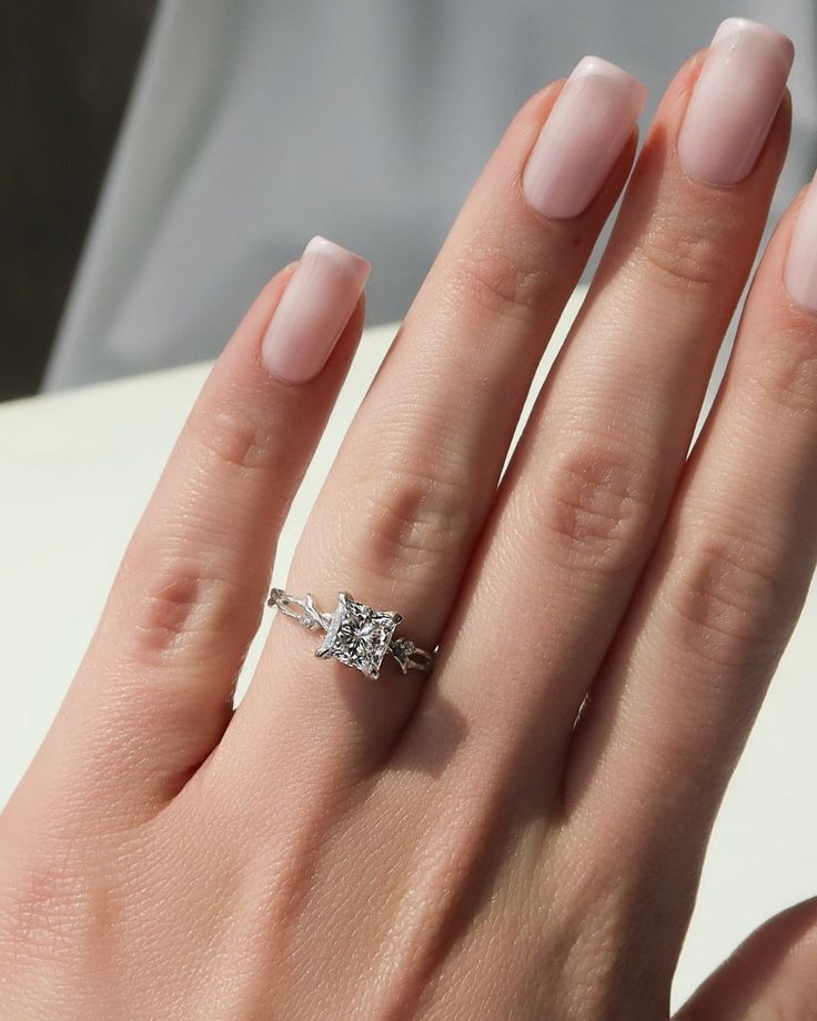 a woman's hand with a diamond ring on her left hand and the other hand holding an engagement ring