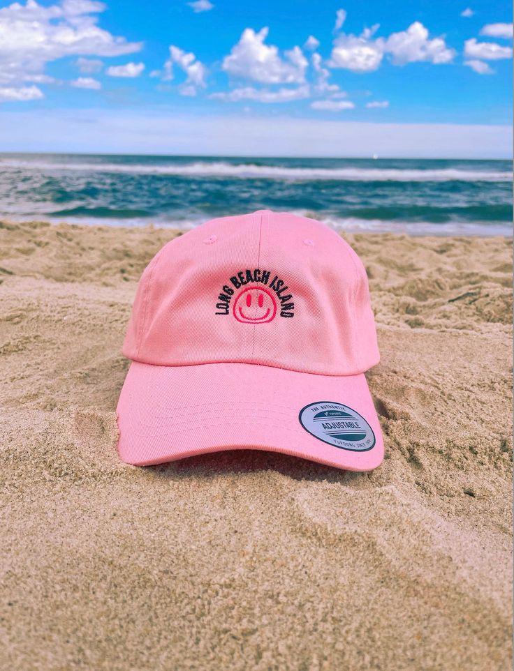 "Rep one of our favorite beach towns with this trendy hat!  This hat style features our Smile graphic and a low profile with an adjustable strap and curved visor. Perfect for those sunny beach days! This embroidered black and pink design comes in: Pink, Light Blue, Stone, Khaki, and White. Item Features: * 100% chino cotton twill * Unstructured, 6-panel, low-profile * 6 embroidered eyelets * 3 ⅛\" (7.6 cm) crown * Adjustable strap with antique buckle *Please note: Color may differ slightly from how it appears on your screen due to varying monitor settings.  Some designs may come with a white paper backing on the inside of the embroidered design, this is needed during the creation process to ensure the strength and longevity of the design. This product is made especially for you as soon as Adjustable Fit Beach Cap, Casual Adjustable Hat For Beach Season, Adjustable Cap For Beach, Adjustable Beach Cap, Adjustable Curved Brim Hat For Sunbathing, Trendy Adjustable Sun Hat, Adjustable Fit Beach Sun Hat Cap, Adjustable Fit Sun Hat Cap For Beach, Trendy Hats With Uv Protection For Beach Season