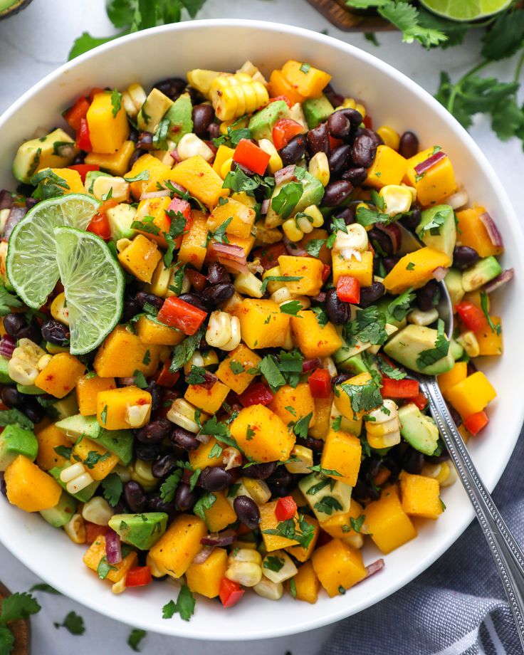 a white bowl filled with black beans, mangoes and avocado garnished with cilantro