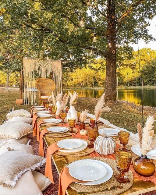 an outdoor table set with plates and place settings for dinner on the grass next to a lake