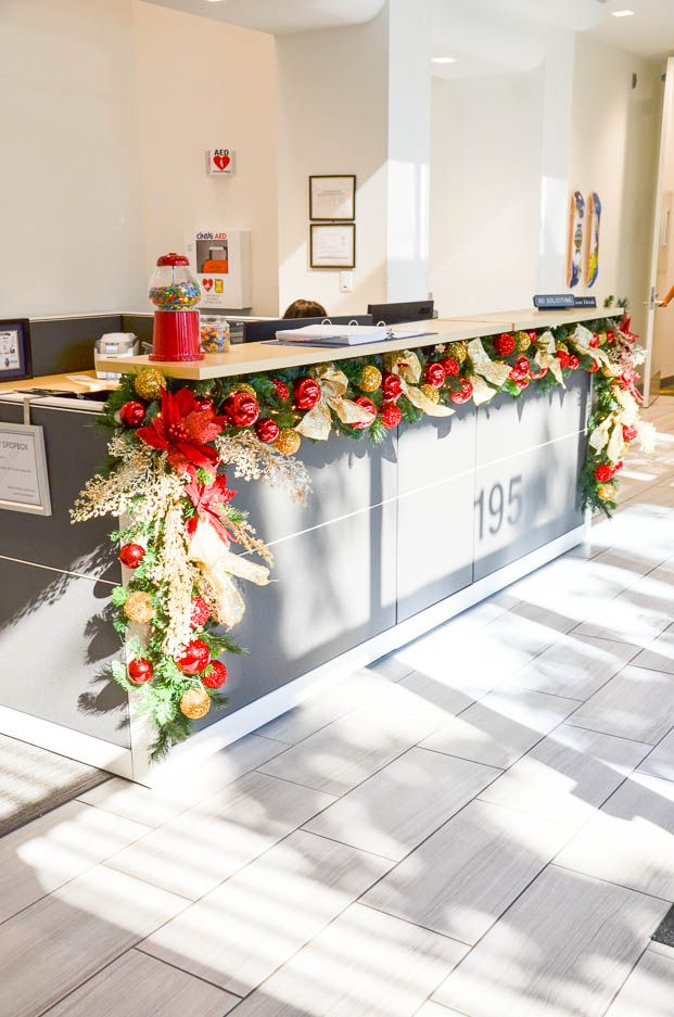 an office decorated for christmas with red and gold decorations on the desks, along with garland