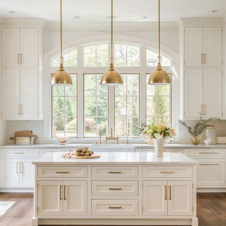 a large kitchen with white cabinets and gold pendant lights hanging from the ceiling over the island