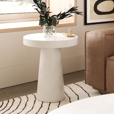 a small white table with some plants on it in front of a couch and window