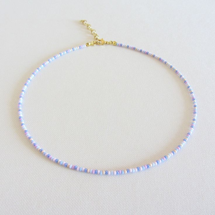 a white beaded necklace with blue beads on a gold plated chain is shown