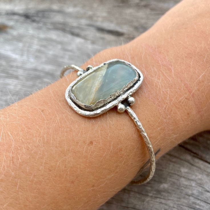 Sterling silver aquateen cuff. Hand made with love! The aquateen has a smooth finish and the silver outline is rather rough, giving the cuff an organic and natural touch. Cuff width: 65 mm (slightly adjustable) Gemstone height: 28mm Gemstone width: 18mm Take a look at our Pebbles & Chance ETSY store https://www.etsy.com/es/shop/pebblesandchance to combine it with other unique, raw, beautiful, precious pieces! Follow us on Instagram! https://www.instagram.com/pebblesandchance/?hl=es Sterling Silver Spiritual Cuff Bracelet With Gemstone, Artisan Gemstone Bangle Gift, Unique Sterling Silver Gemstone Bangle, Unique Sterling Silver Bangle With Gemstone, Artisan Gemstone Bangle For Gift, Everyday Silver Hand Wrapped Jewelry, Everyday Hand Wrapped Silver Jewelry, Adjustable Sterling Silver Cuff Bracelet With Gemstone, Adjustable Sterling Silver Cuff Bracelet With Natural Stones