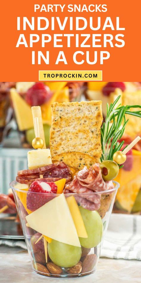 an appetizer in a cup with cheese, crackers and fruit