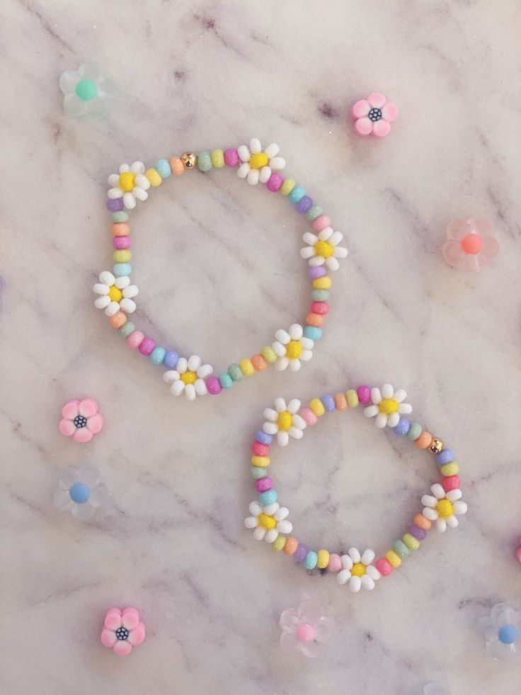 two bracelets with flowers on them sitting on a marble surface next to other beads