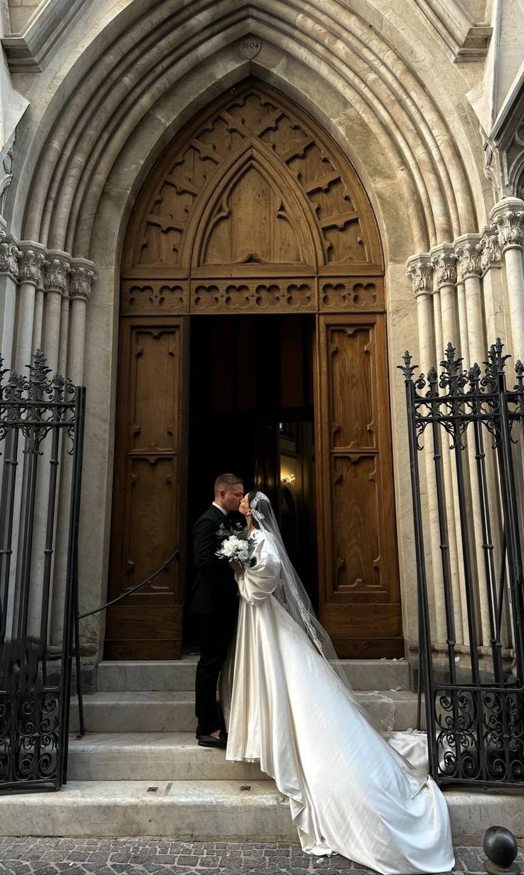 a bride and groom standing in front of an ornate doorway with wrought iron railings