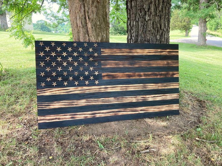 an american flag made out of wood sitting in the grass next to a large tree