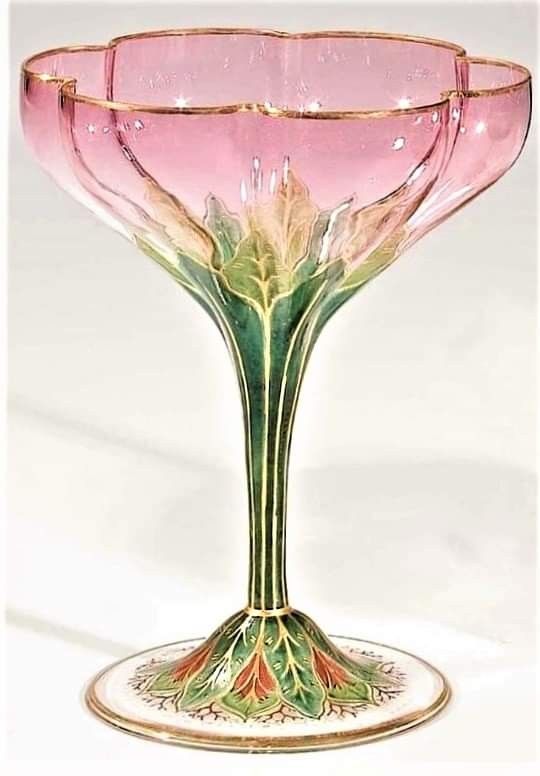 a pink glass vase sitting on top of a white table next to a green and gold plate