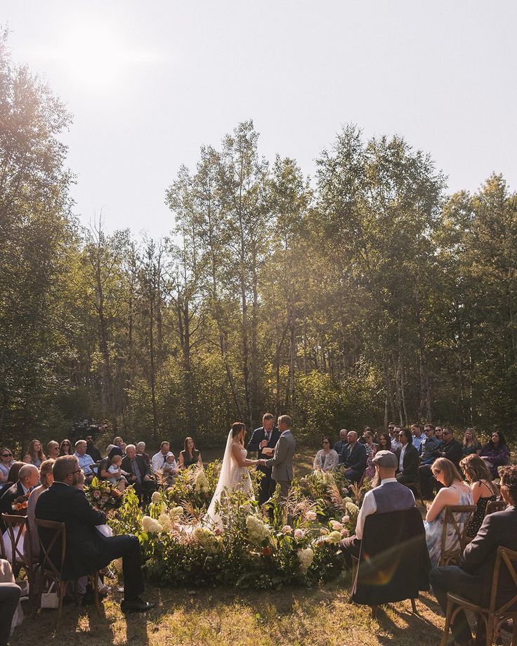 a bride and groom standing in front of an outdoor wedding ceremony with guests seated on lawn chairs