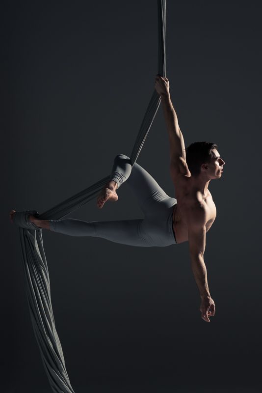 a shirtless man doing aerial acrobatic tricks on a pole with one leg