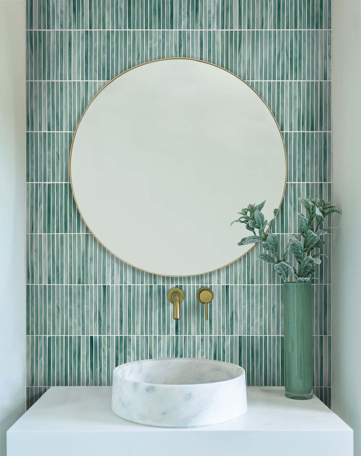 a round mirror sitting on top of a white counter next to a vase with plants