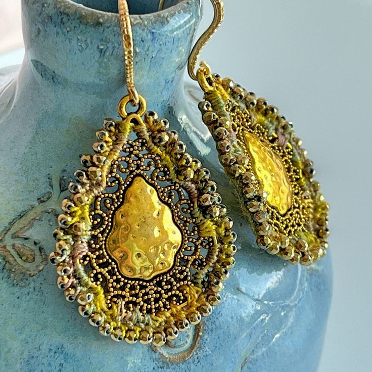 These eye-catching drop earrings feature ornate, antique gold-plated teardrops - with a hammered metal center and a scrolling filigree border. I embellished the edges with crochet using hand-dyed, cotton thread in shades of golden yellow, sage green, and taupe and tiny, faceted, metallic gold glass beads.  These earrings shimmer with reflected light.  They are finished with half-hammered, gold-plated brass (nickel and lead free) ear wires.  These earrings hang to a length of 2 1/4 inches.  The drops are 1 1/2 inches long and about 1 1/8 inches wide.  One of a kind beauties! Metal Teardrop Jewelry With Intricate Design, Antique Gold Chandelier Earrings In Brass, Antique Gold Dangle Chandelier Earrings, Artisan Gold Teardrop Pendant Jewelry, Antique Gold Chandelier Dangle Earrings, Antique Gold Chandelier Earrings Gift, Antique Gold Chandelier Earrings For Gift, Antique Gold Metal Chandelier Earrings, Bohemian Gold Chandelier Earrings For Festival