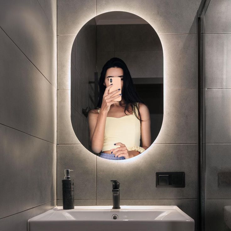 a woman taking a selfie in front of a bathroom mirror with her cell phone