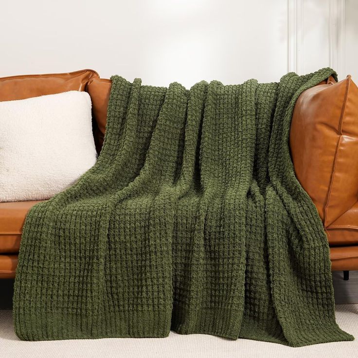 a couch with a green blanket on top of it next to a pillow and pillows