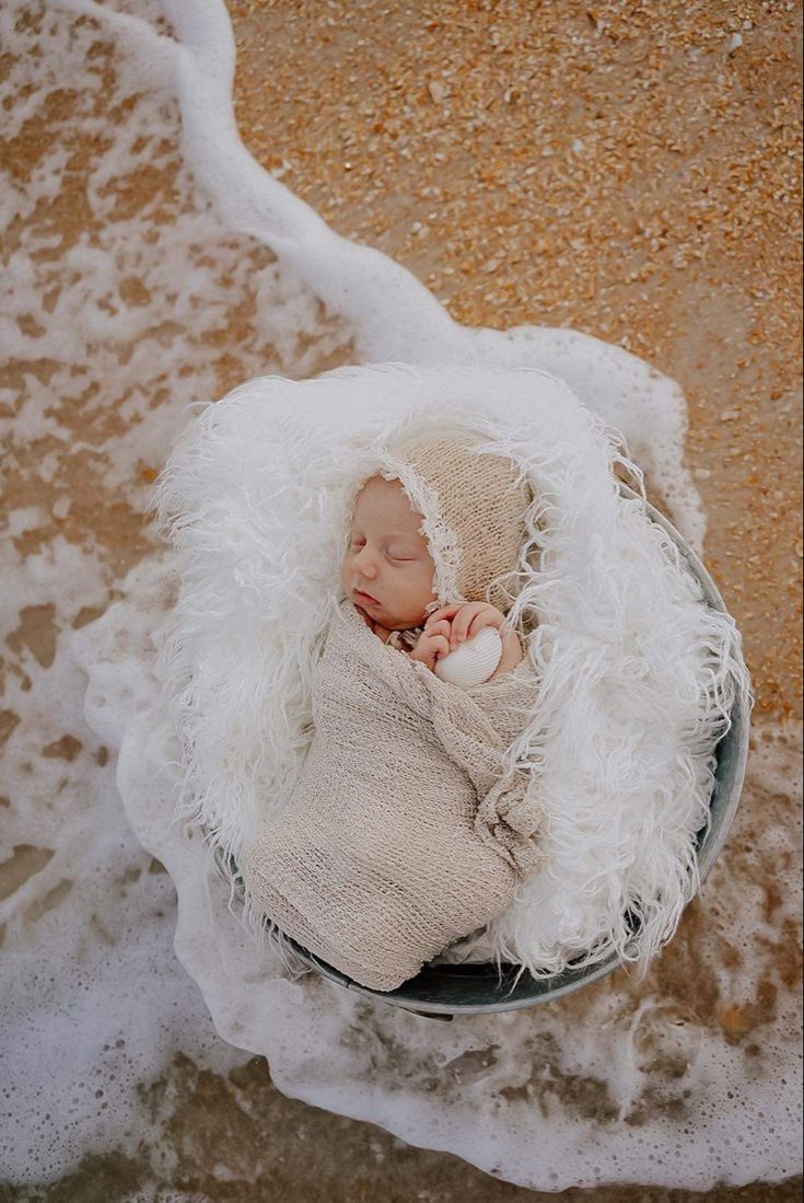 a newborn baby wrapped in a blanket is laying on a metal bowl with snow around it