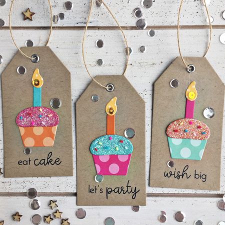 three birthday tags with cupcakes on them hanging from strings and confetti sprinkles