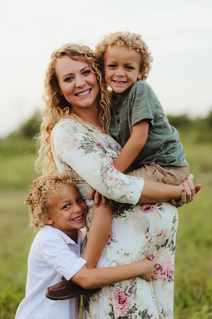 a woman and two children hugging each other in the middle of an open field with grass