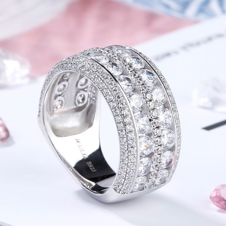 Celebrate your everlasting love story with this elegant band. Stunning as a wedding or anniversary band, two rows of sparkling round stones are set across the center of this band and split by a row of smaller round stones - decorates the ring's impressive shank. A double row of smaller round stones grace the top and bottom of the band, completing this exceptional design. This band is a beautiful reminder of your timeless romance.Carat Weight: 6.575 ctStone Size: 3,1,1.2 mmStone Type: Jeulia® Sto Cubic Zirconia Eternity Band With Pave Setting For Wedding, Wedding Rings In Diamond White With Rhinestones, Diamond White Wedding Rings With Rhinestones, Silver Bands With Diamond Accents In Cubic Zirconia, Silver Bands With Diamond Accents And Cubic Zirconia, Cubic Zirconia Rings With Rhinestones For Anniversary, Anniversary Rings With Cubic Zirconia And Rhinestones, Dazzling Diamond Ring With Rhinestones For Anniversary, Classic Rings With Bling For Anniversary