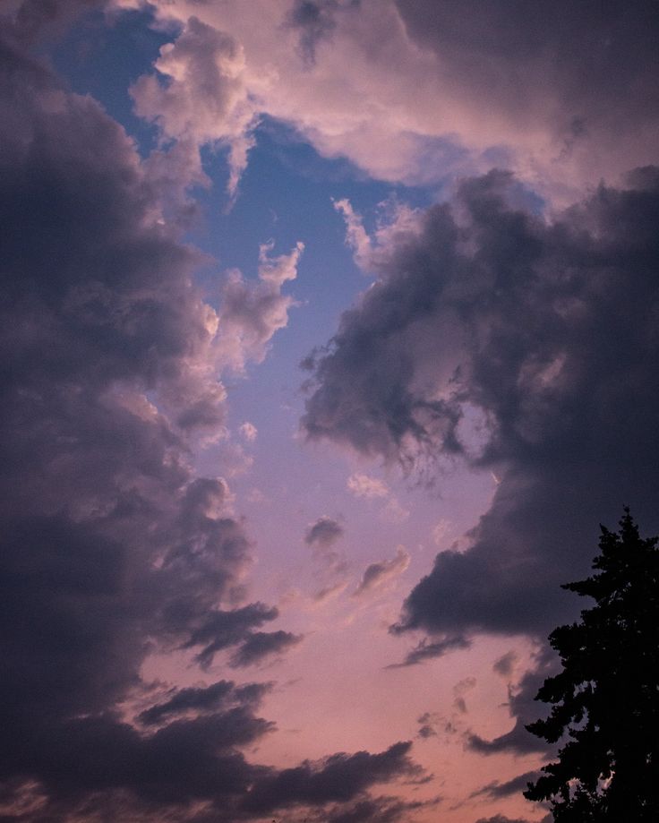 the sky is filled with dark clouds and some trees in front of an orange sunset