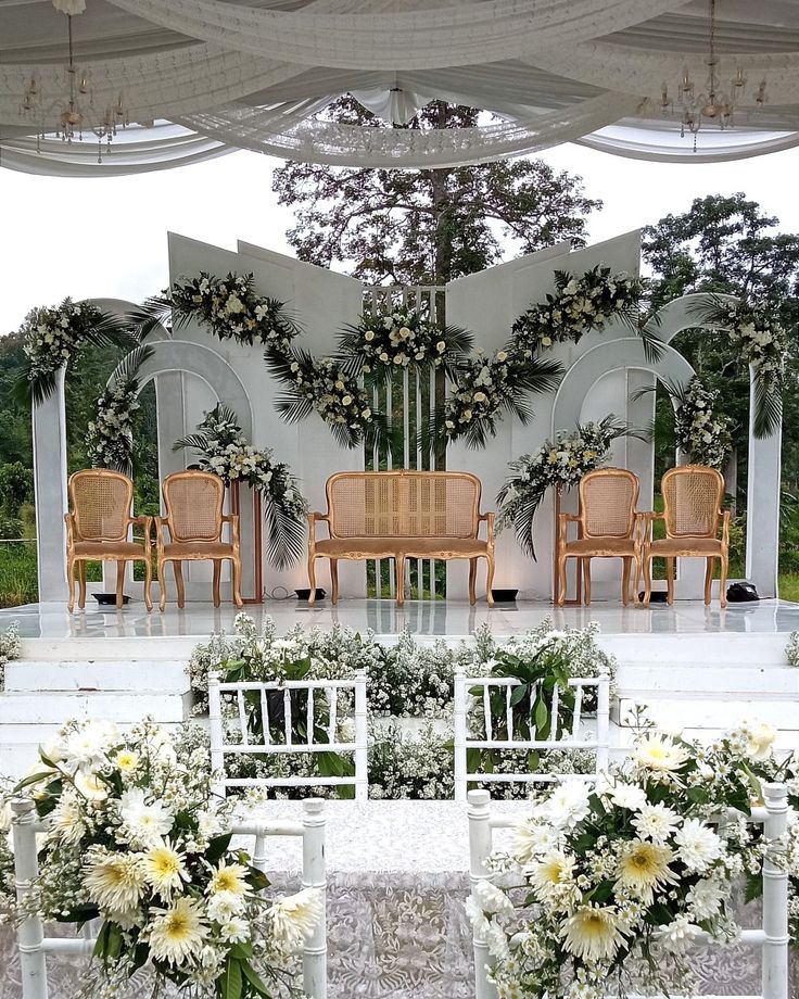 an outdoor wedding setup with white flowers and greenery on the back wall, set up for a ceremony