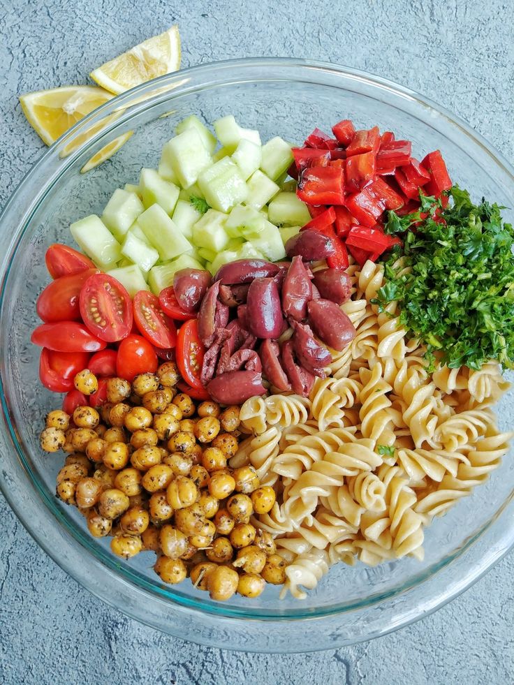 a bowl filled with pasta and vegetables on top of a blue tablecloth next to a lemon wedge