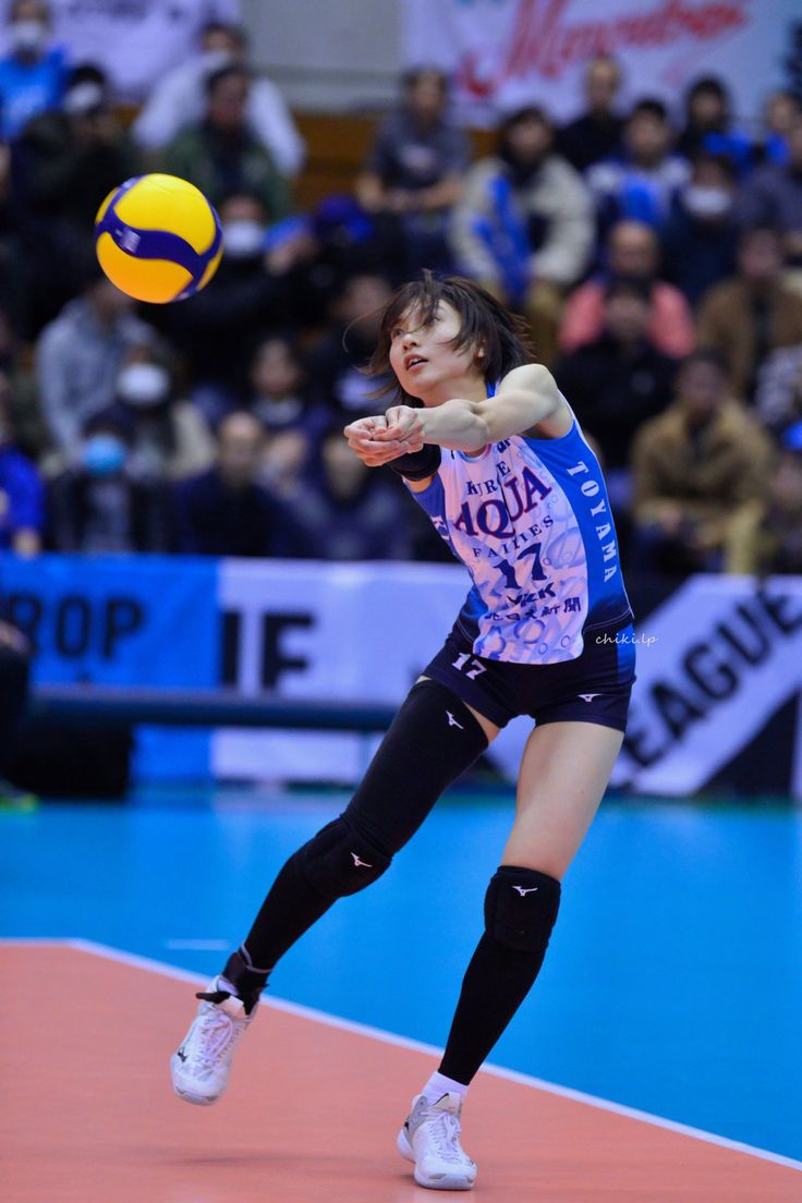 a female volleyball player in action on the court with a ball above her head and spectators watching