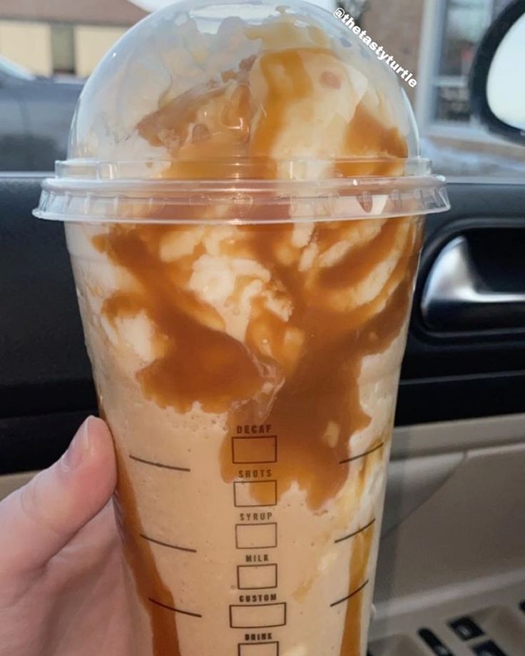 a hand holding up a cup filled with ice cream and caramel on the inside