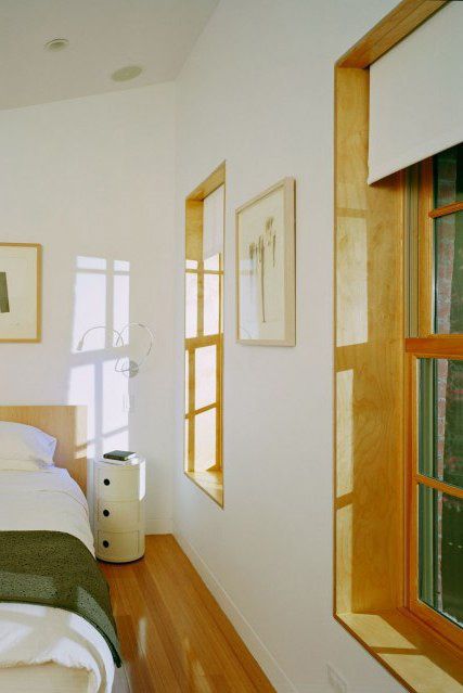 a bedroom with white walls and wood flooring next to a bed in front of two windows