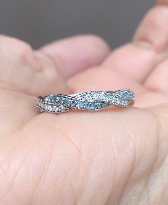 a woman's hand holding a wedding ring with blue and white diamonds