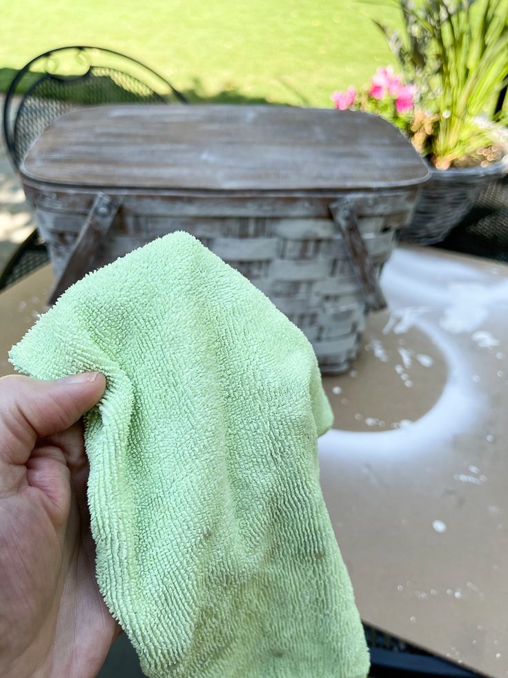 a hand holding a green micro towel over a table with a basket in the background