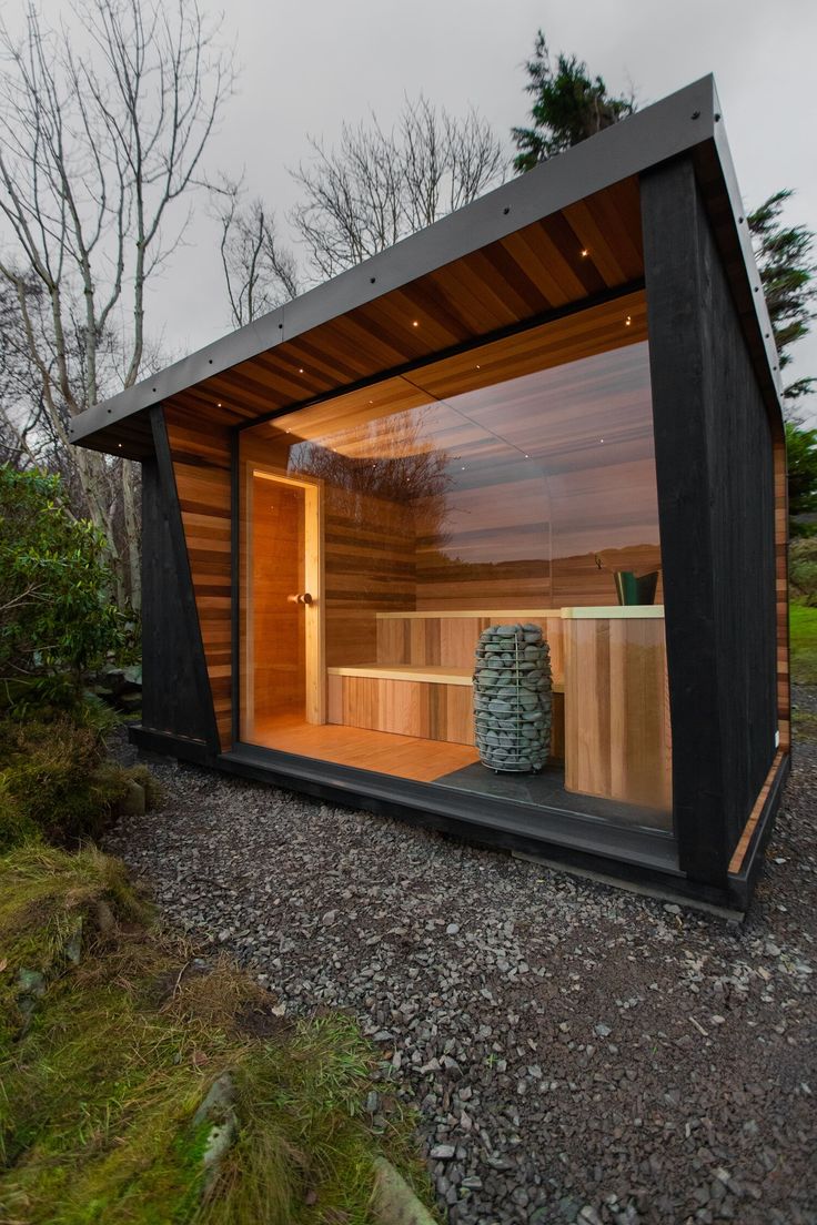 an outdoor sauna in the middle of a gravel area with rocks and grass around it