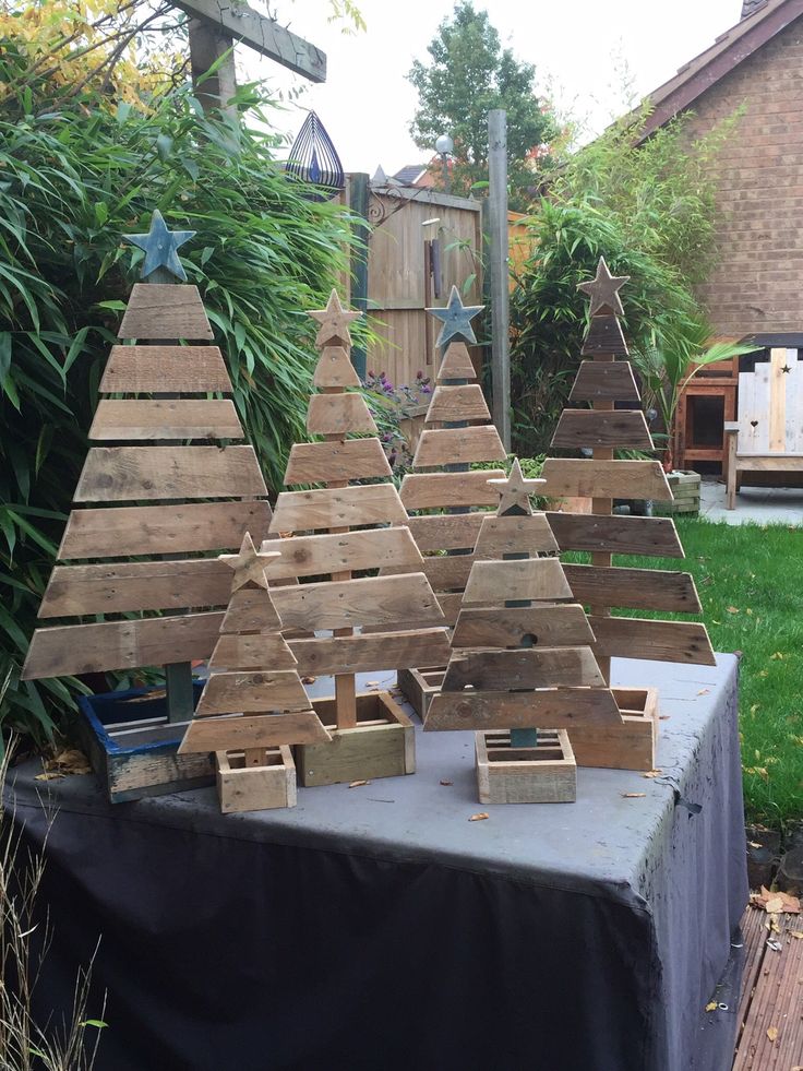 several wooden christmas trees sitting on top of a table in the grass next to a fence