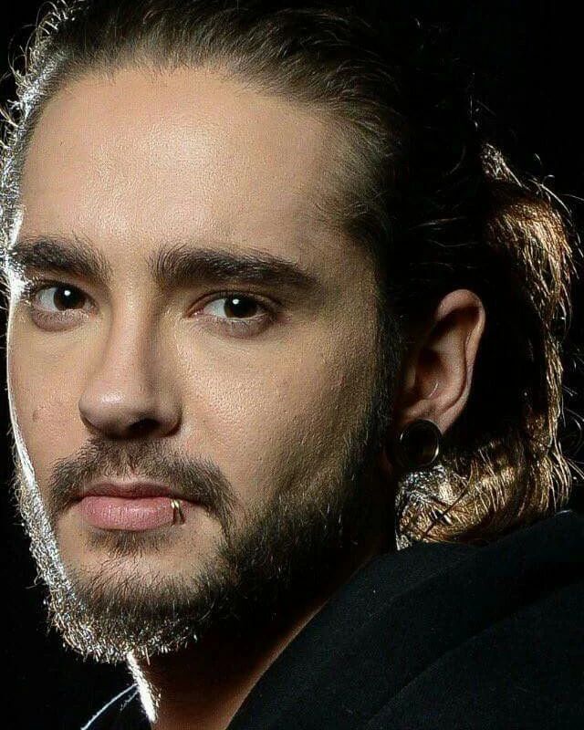 a close up of a person with long hair and piercings on his ears, looking at the camera