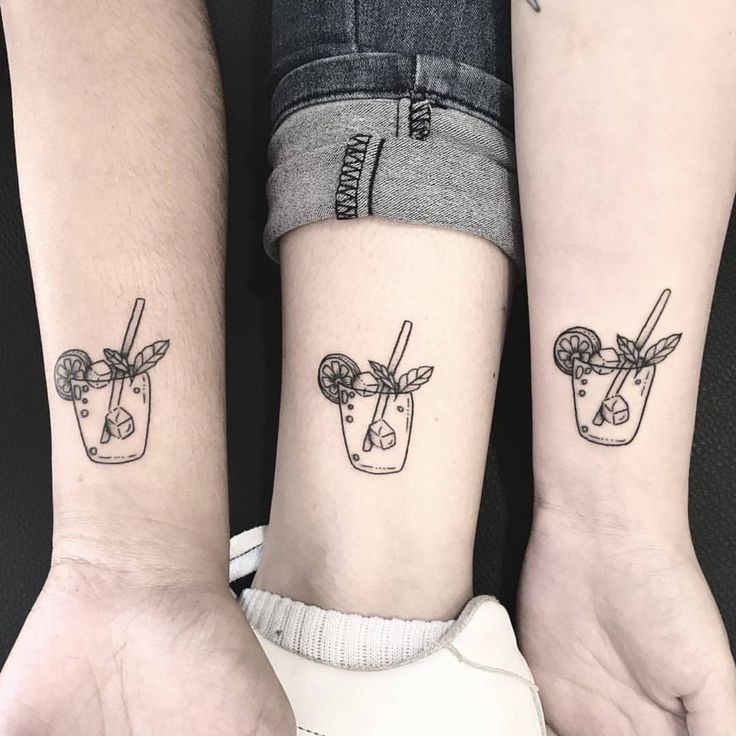 two people with matching tattoos on their arms holding each other's hands, one has a drink and the other has a straw