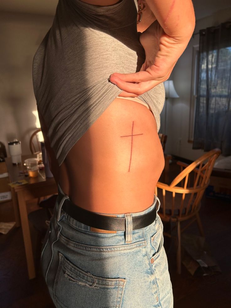 a woman with a cross tattoo on her back, standing in front of a table