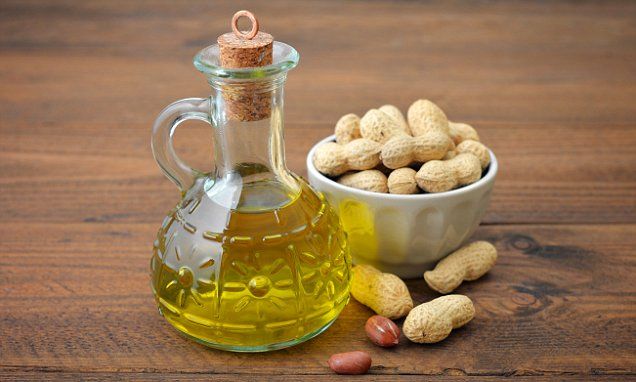 a bottle of almond oil next to a bowl of peanuts